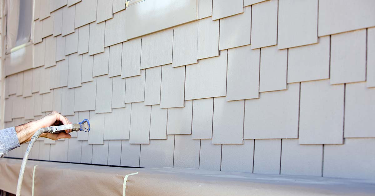 Professional house painter spraying paint on newly prepped siding for a long-lasting exterior finish