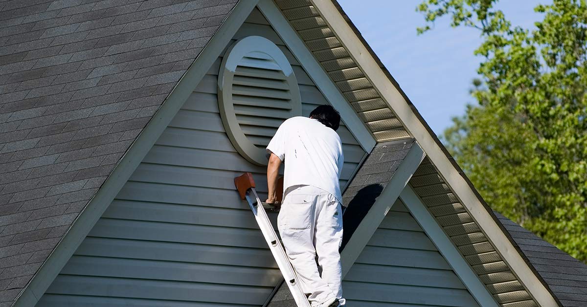 Professional painter applying exterior paint to home siding, demonstrating the importance of proper timing, surface temperatures, and weather conditions for long-lasting results.
